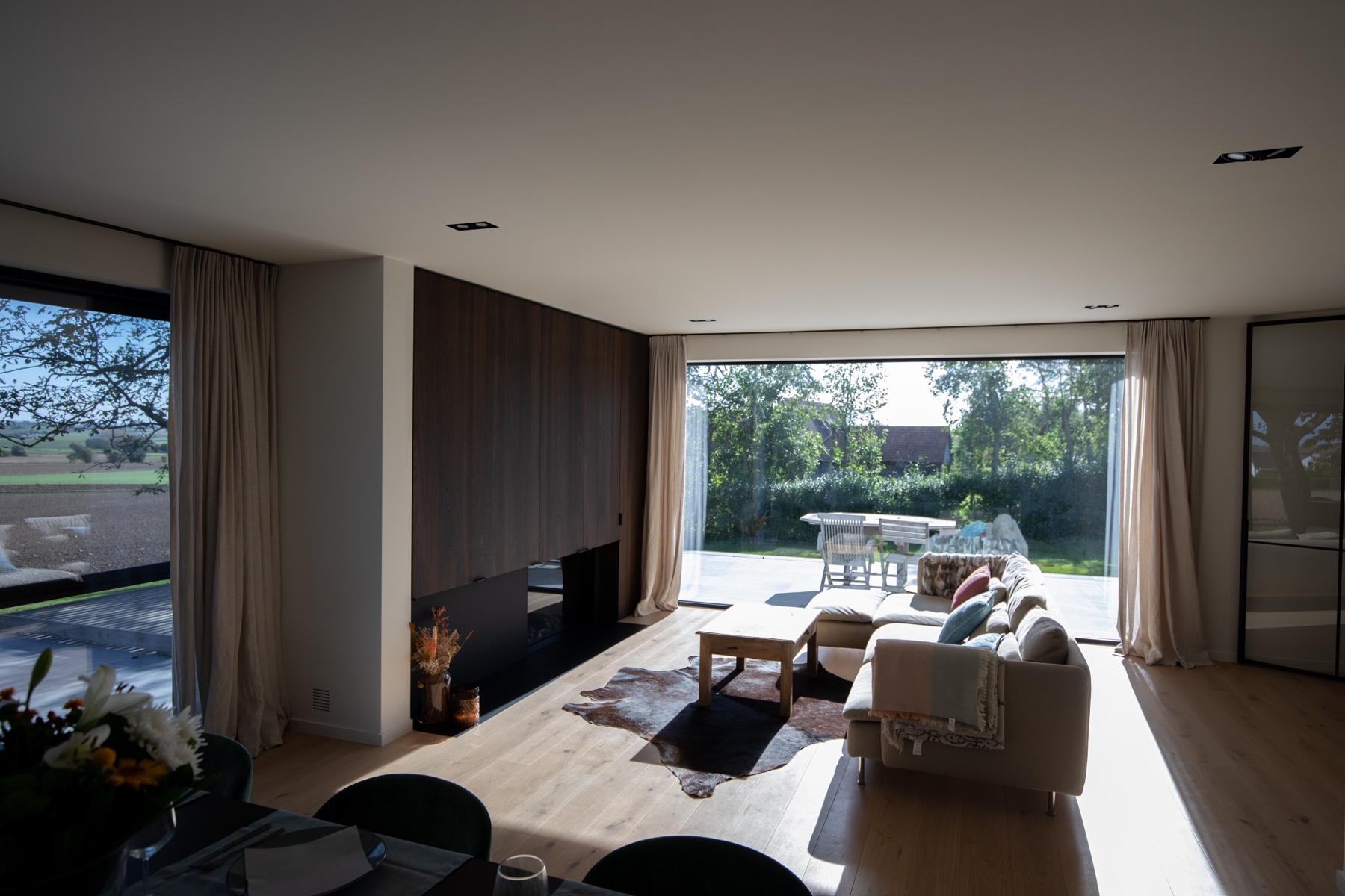 Leefruimte met houten haardwand en brede opening naar de tuin