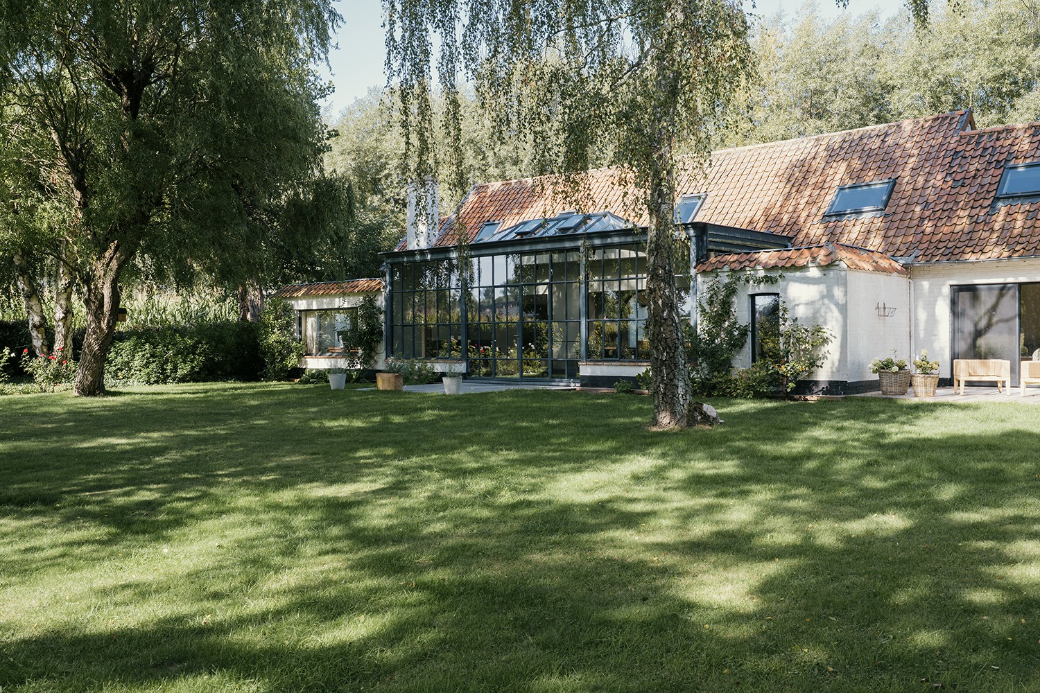 De witgeschilderde woning en glazen serre gezien vanuit de groene tuin