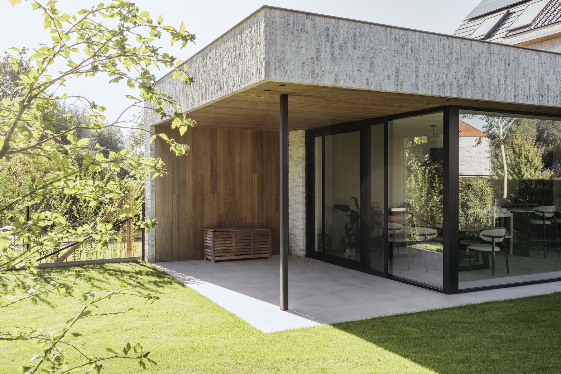 Tuinuitbreiding van House T met glas, hout en een brede gemetselde luifel