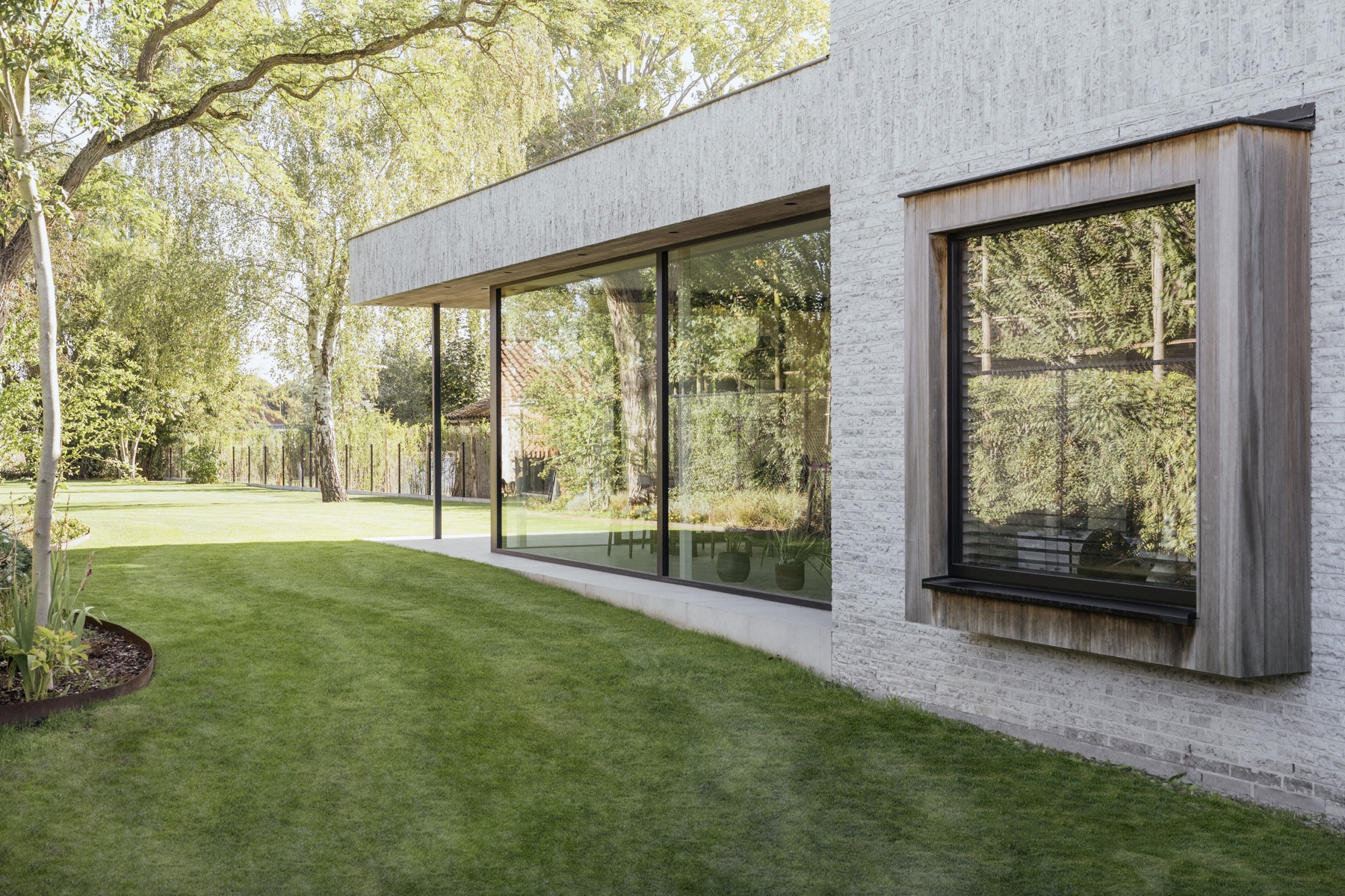 Glaswand en houten raamomlijsting van House T met de weerspiegeling van de tuin