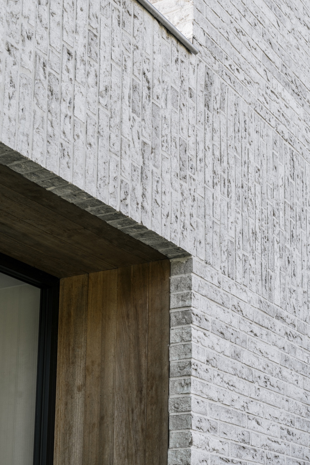 Detail van het lichte metselwerk, de gemetselde luifel en houten bekleding van House T