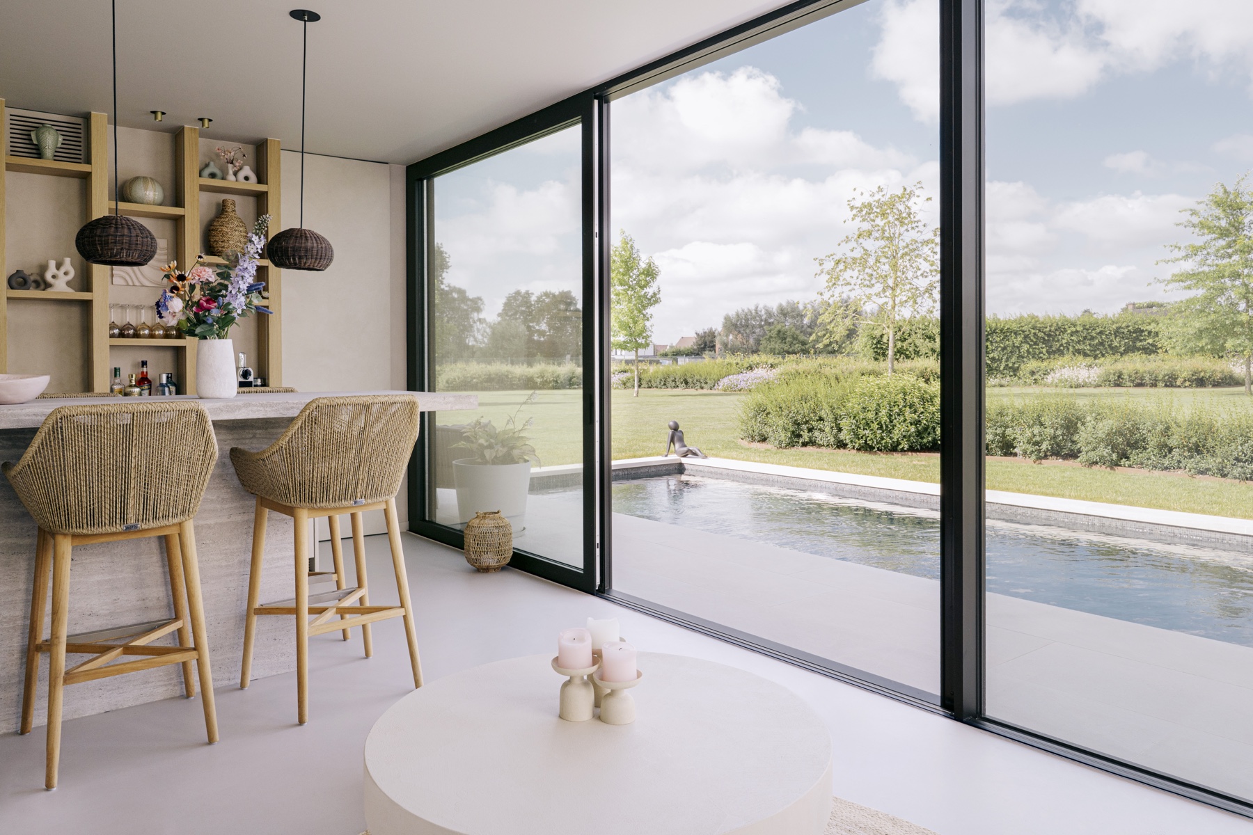 Interieur van Poolhouse V met houten barstoelen, natuurstenen bar en brede glaswand naar zwembad en tuin